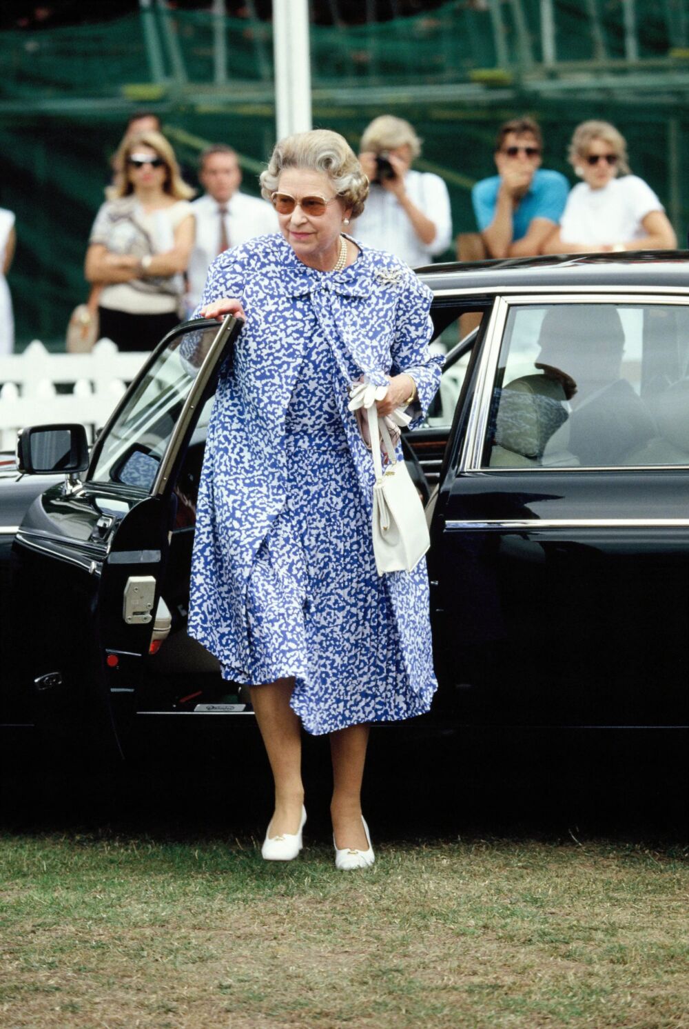 1990 - A a bow-necked dress and coat with white accessories and sepia sunglasses at the 1990 Cartier Queen’s Cup
