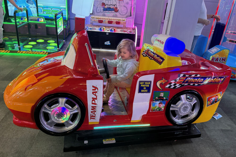 A young girl sitting inside a red "Photo Motion" toy car ride at the resort arcade.
