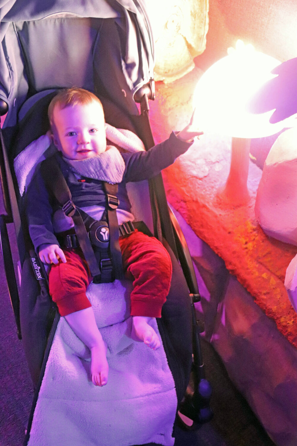 A baby strapped into a stroller looking at a glowing light feature in the resort lobby.
