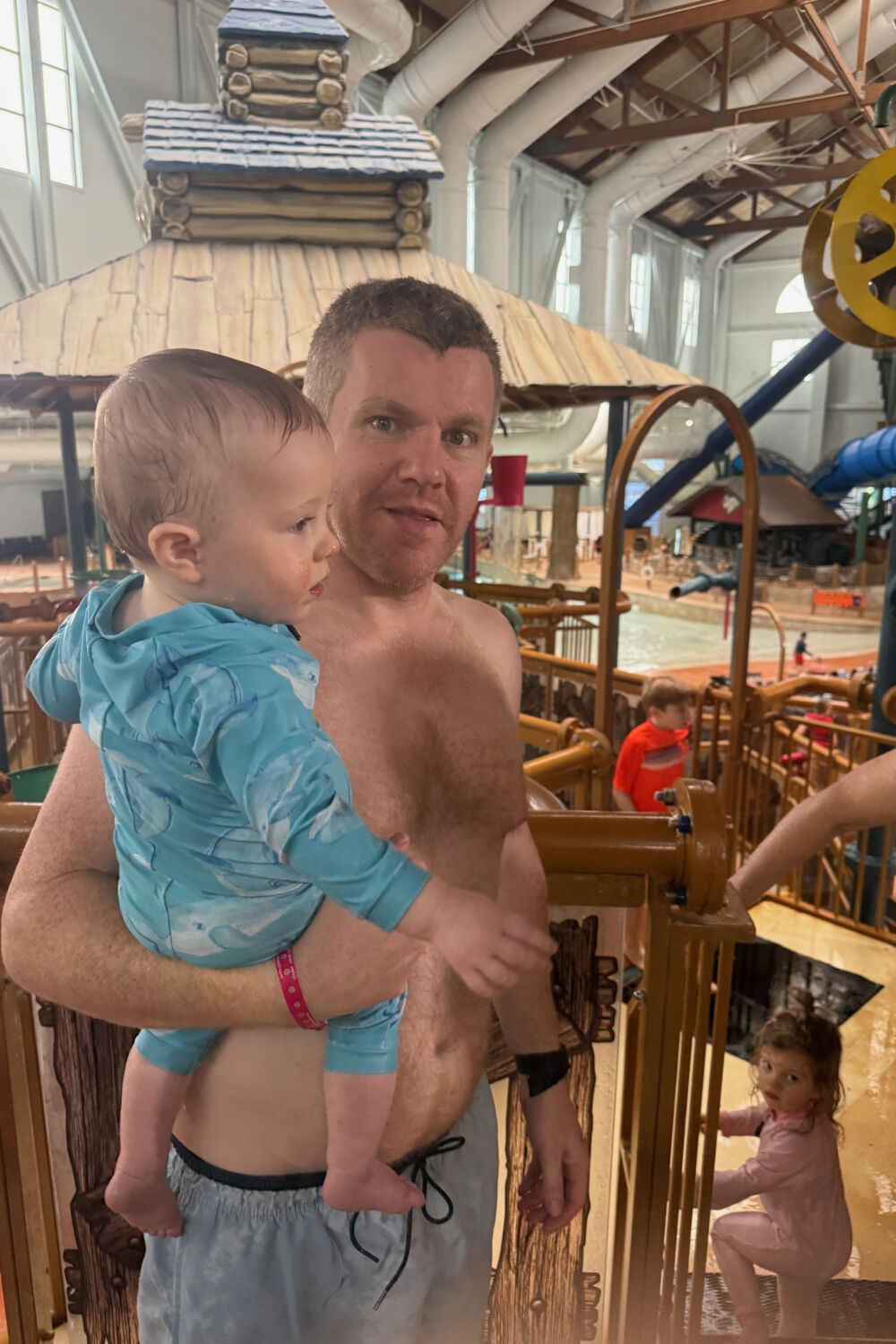 A father holding his baby while overlooking the active indoor waterpark.