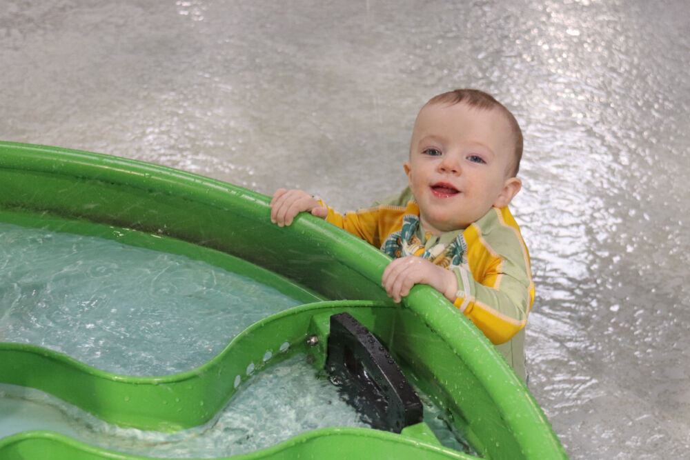 A 13-month-old toddler playing at a green water sensory table in the Cub Paw Pool splash area.