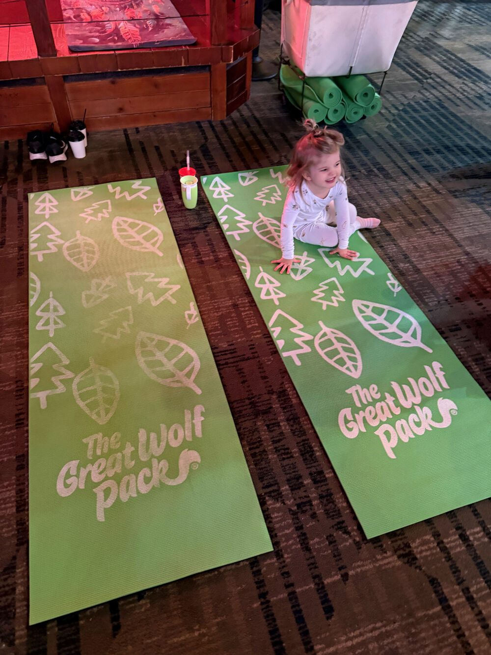 A young girl sitting on a "The Great Wolf Pack" branded yoga mat during a morning session.