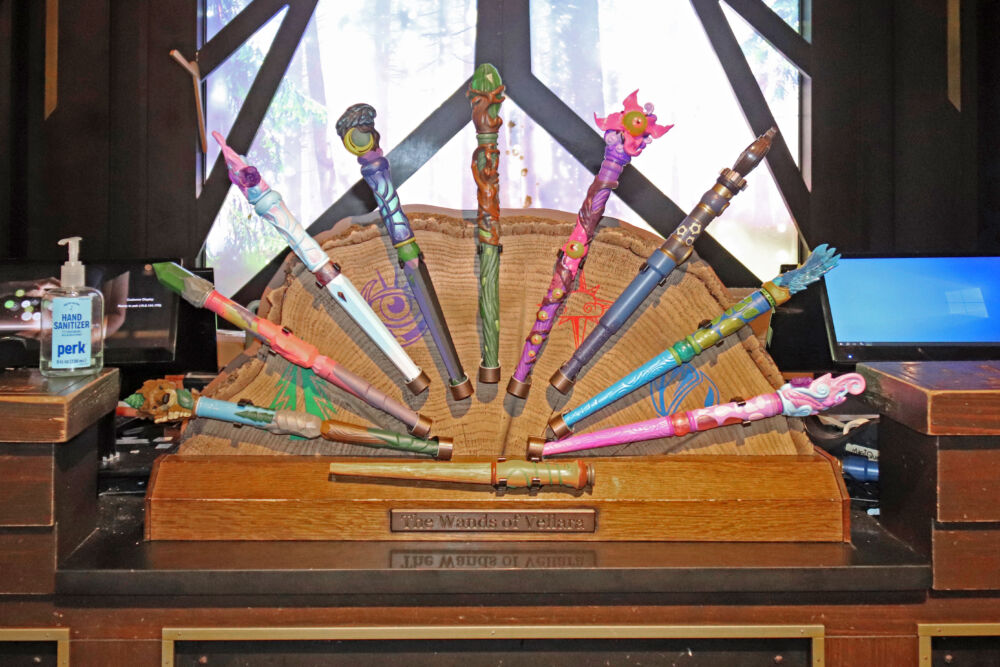 A wooden display case showing a variety of colorful and themed MagiQuest magic wands.