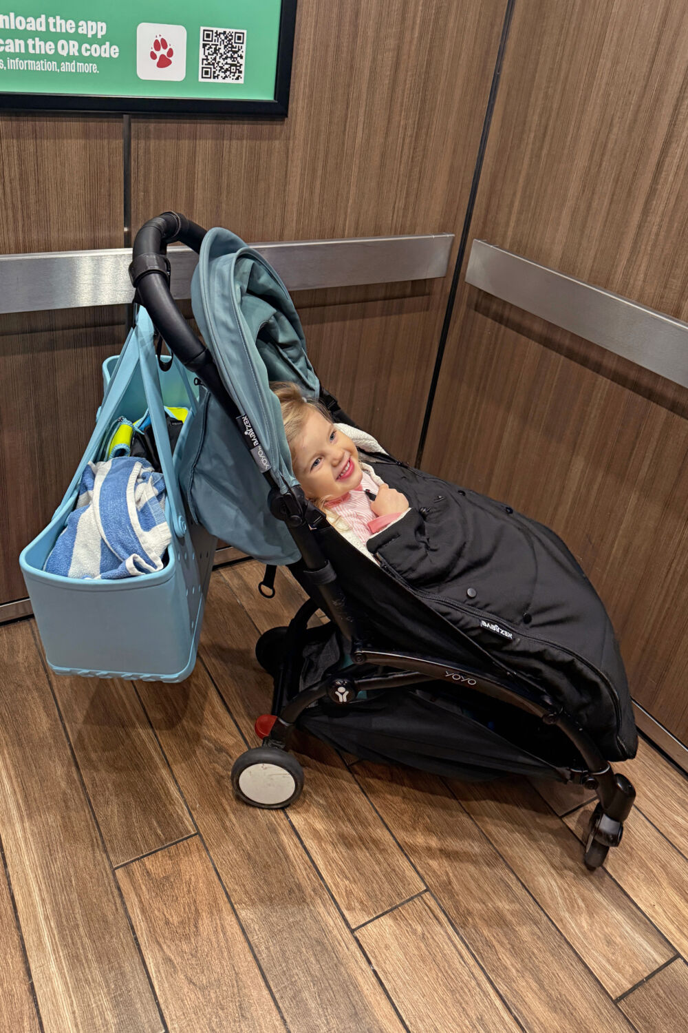 A happy toddler girl sitting in a stroller inside a resort elevator after a day of fun.