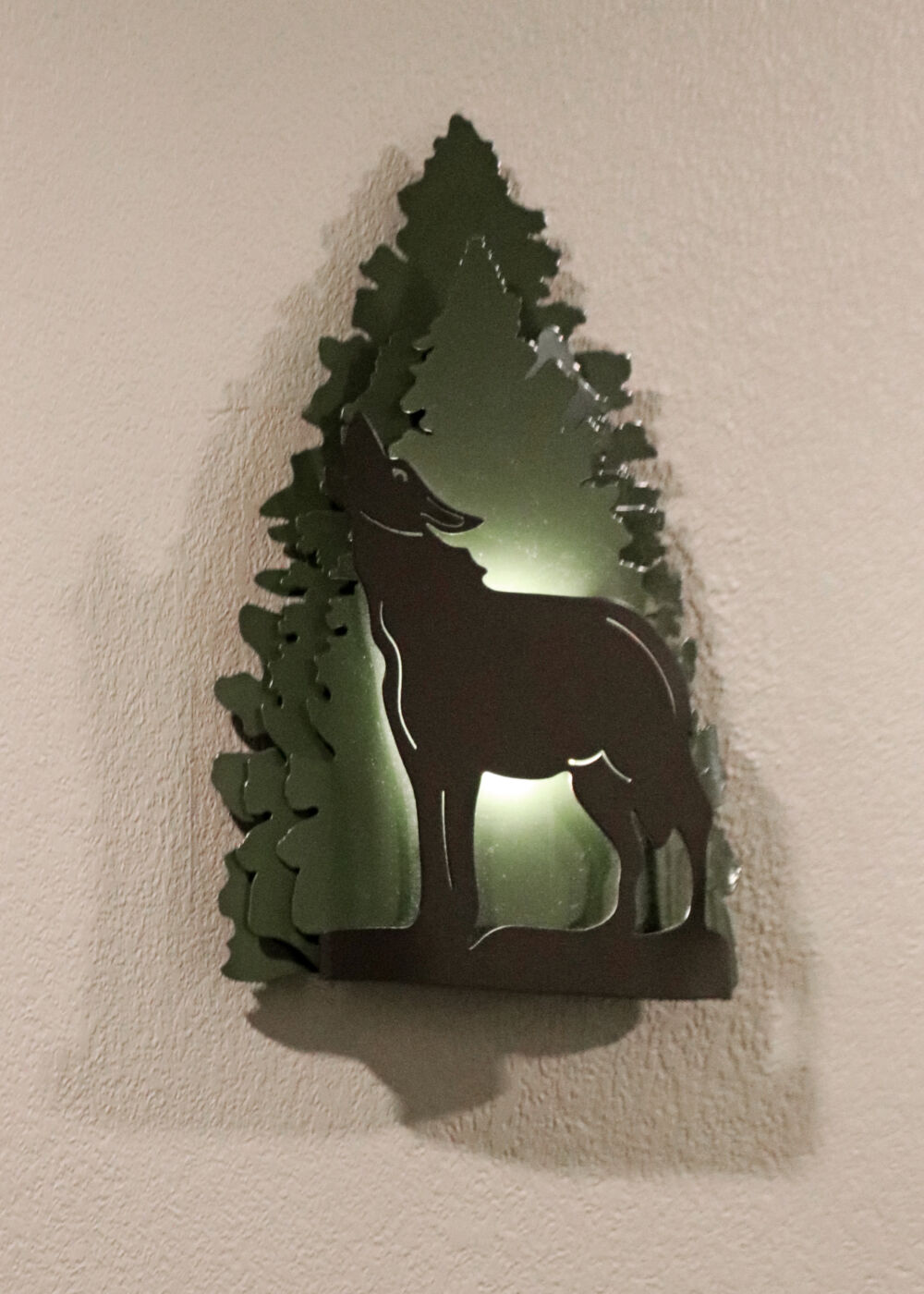A lit-up silhouette of a howling wolf inside a pine tree shape on a resort wall.